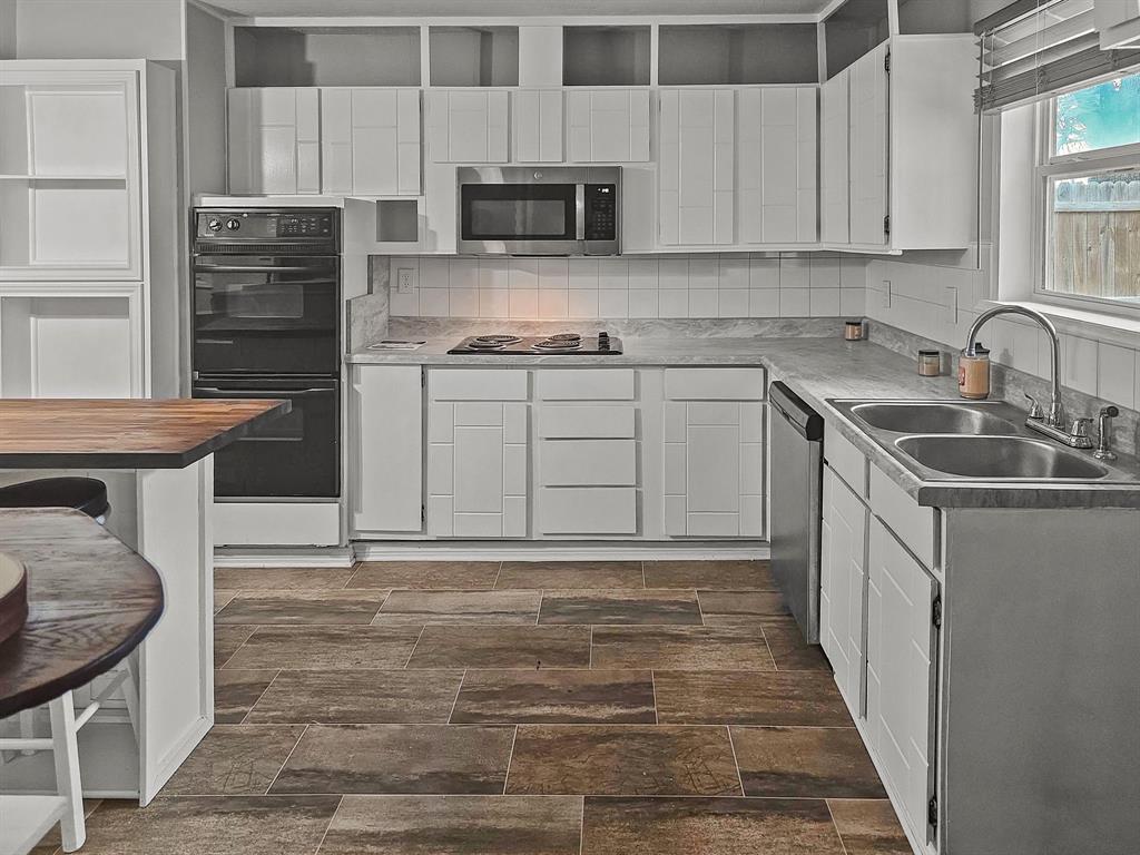 701 Idlewilde Drive Lewisville, TX 75067 - Photo 2 of 13 Kitchen with black appliances, new white cabinetry, tasteful backsplash, and new sink & butcher block island.