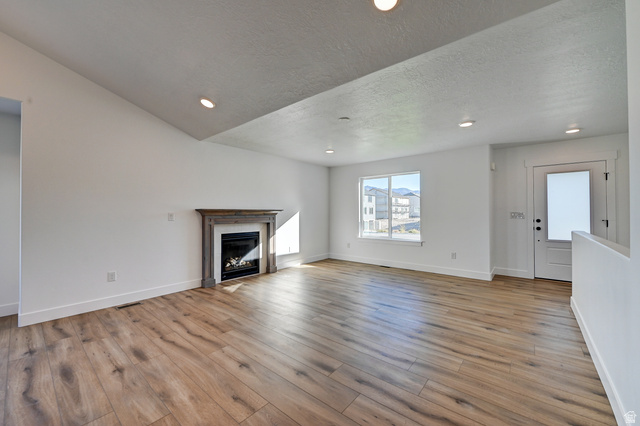 1848 Mantle Way, Unit 417 Tooele, UT 84074 - Photo 2 of 6 Spacious living area featuring wood-finish flooring, a fireplace with a decorative mantel, recessed lighting, and a large window providing ample natural light
