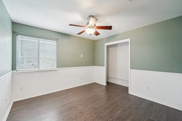 an empty room with wooden floor chandelier fan and windows