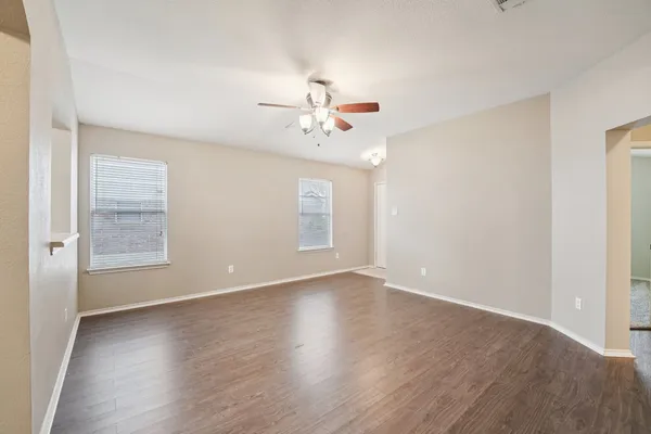 an empty room with wooden floor chandelier fan and windows
