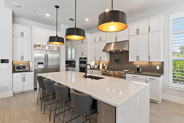 a kitchen with stainless steel appliances granite countertop a refrigerator a sink dishwasher a dining table and chairs with wooden floor