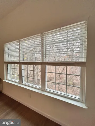 a view of an empty room with wooden floor and a kitchen