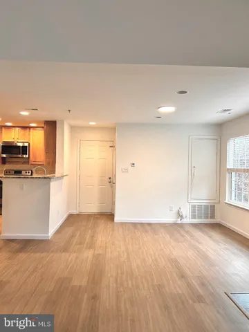 a view of an empty room with wooden floor and a kitchen
