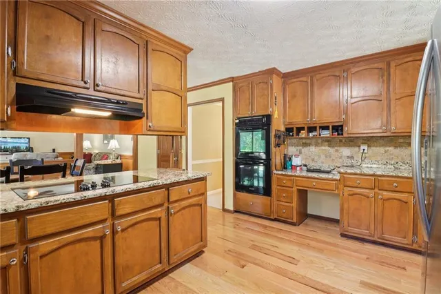 a kitchen with stainless steel appliances granite countertop wooden cabinets a sink and dishwasher a refrigerator with wooden floor