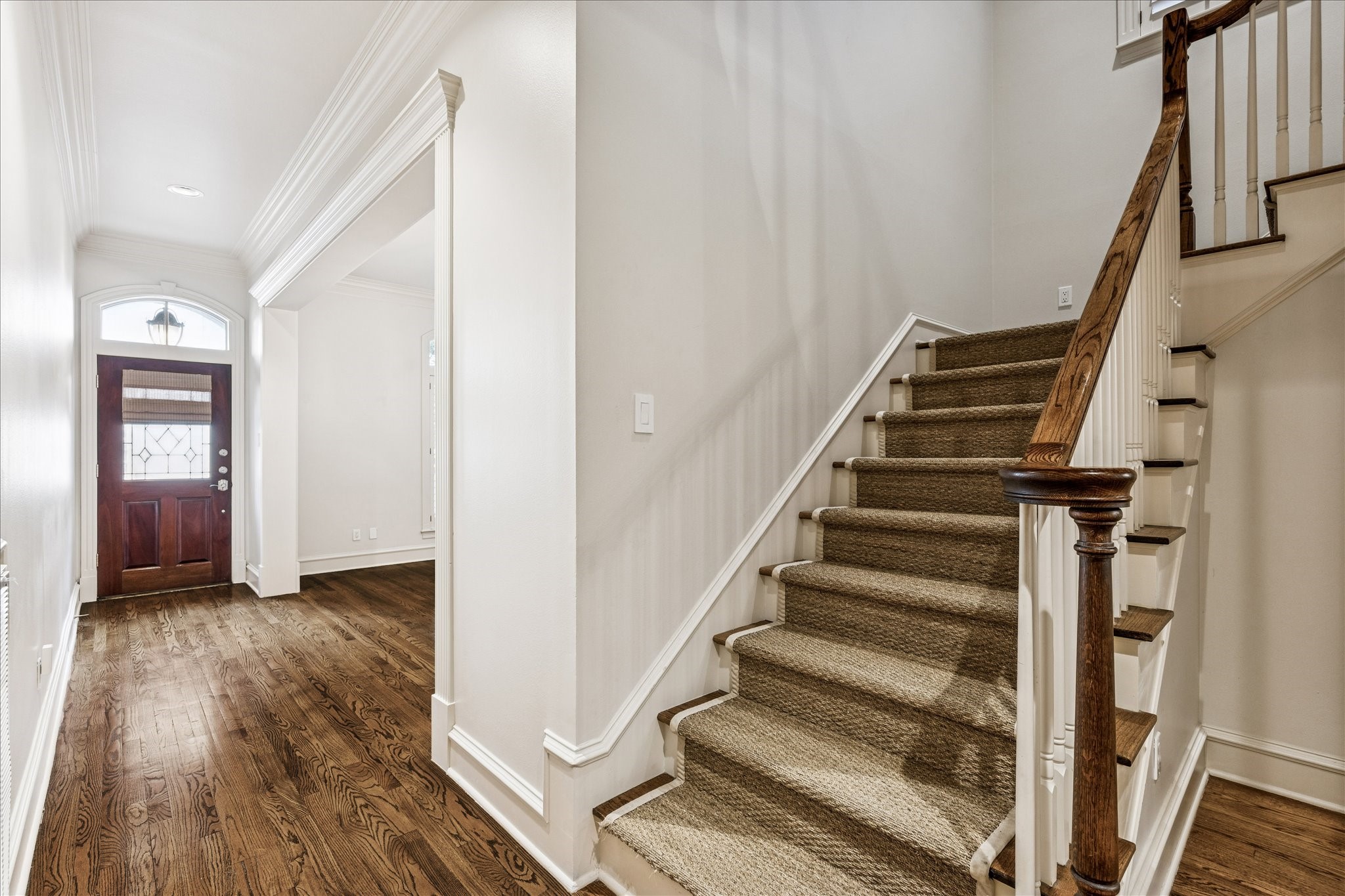 5823 Augusta Court Houston, TX 77057 - Photo 3 of 44 A welcoming entryway with hardwood floors and a carpeted staircase leading upstairs. The front door features decorative glass, and the space is elegantly framed with crown molding.