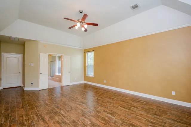 a view of an empty room with wooden floor and a ceiling fan