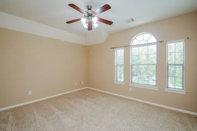 an empty room with chandelier fan and windows