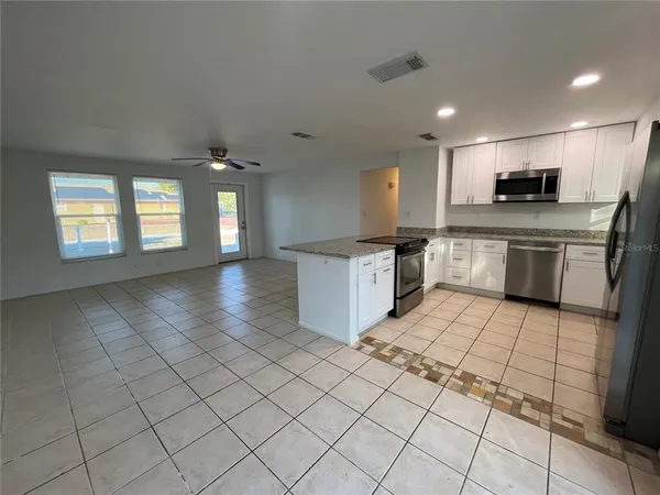 a large kitchen with stainless steel appliances granite countertop a sink and white cabinets