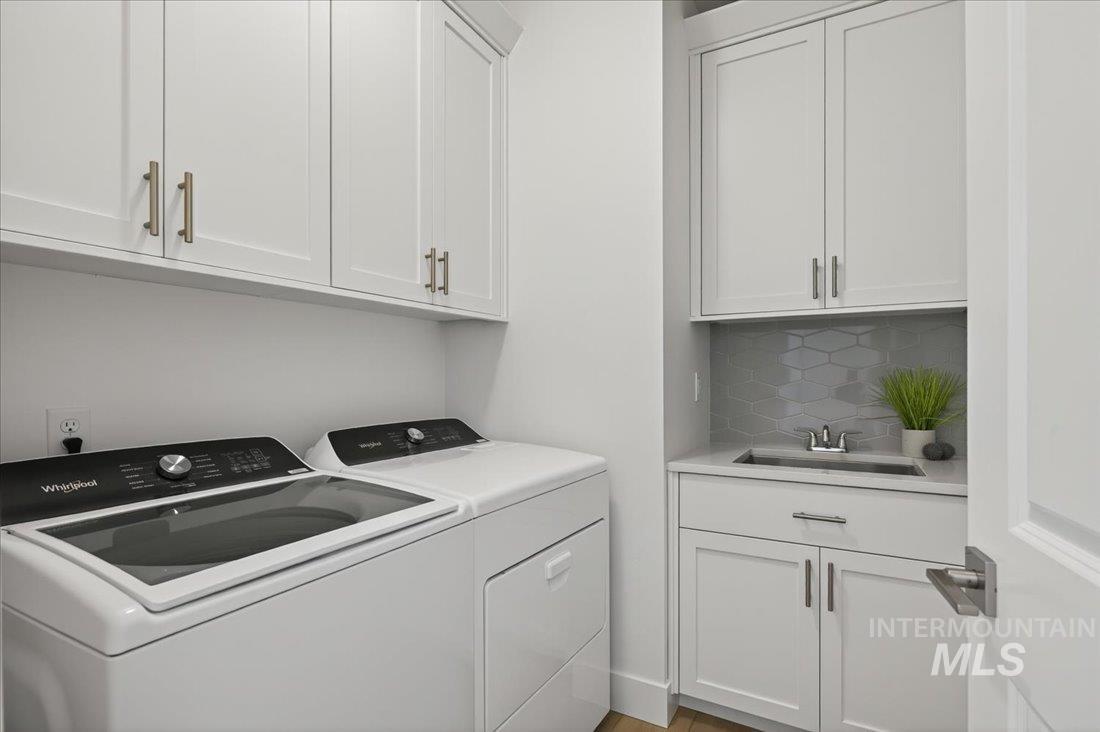 14880 Wing Spread Drive Caldwell, ID 83607 - Photo 11 of 12 Dedicated laundry space featuring white shaker-style cabinetry with brushed nickel hardware, a built-in utility sink with a chrome faucet, light grey hexagonal tile backsplash, and wood-finish flooring