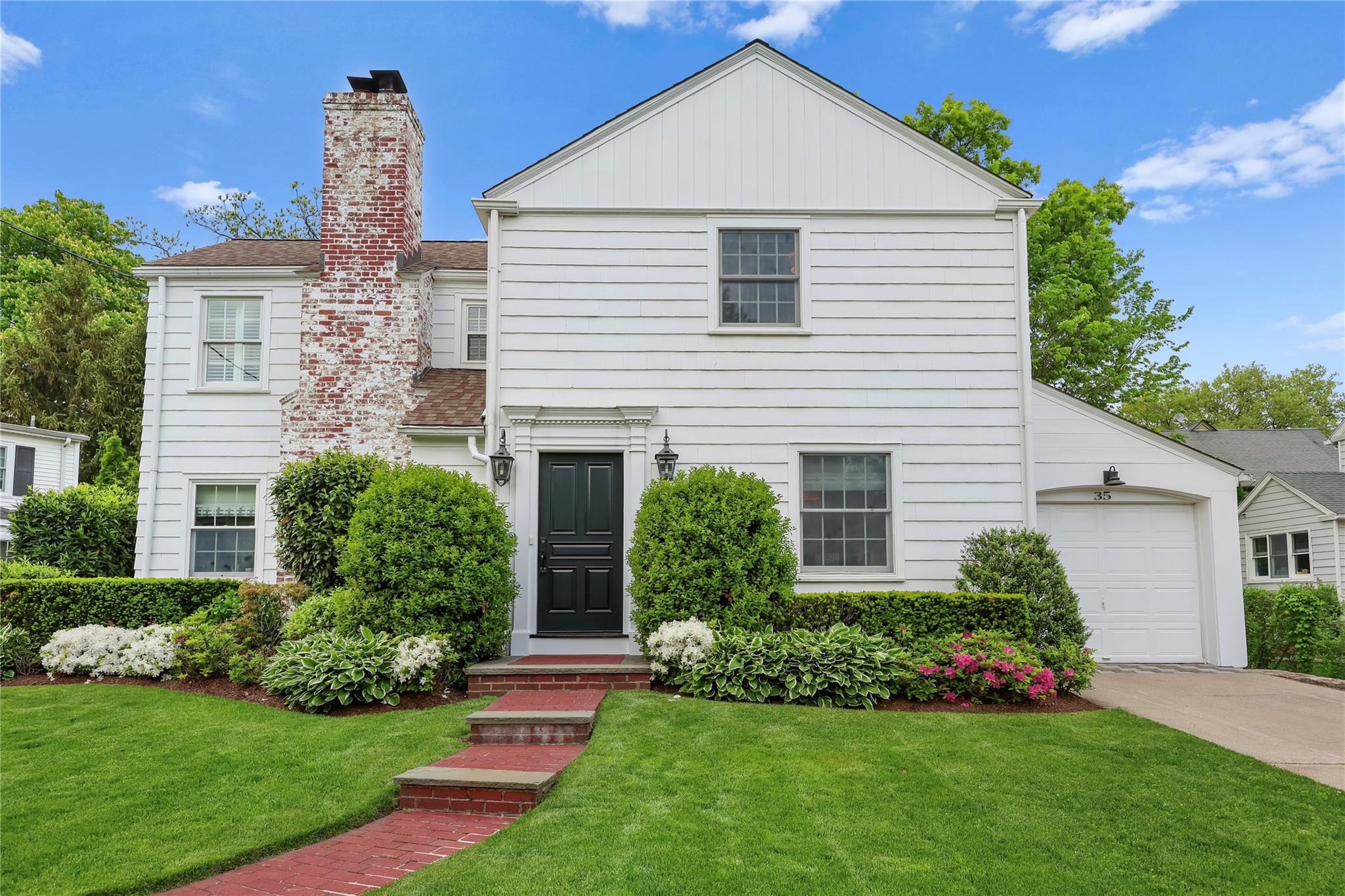 View of front of house featuring driveway, a front lawn, a chimney, and an attached garage