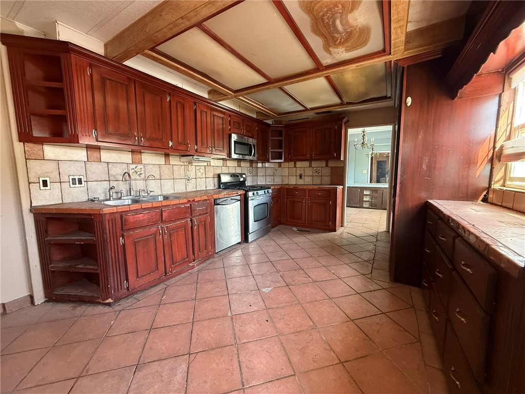 1629 Ramar Road Bullhead City, AZ 86442 - Photo 18 of 29 Kitchen featuring open shelves, tile counters, appliances with stainless steel finishes, light tile patterned floors, and decorative backsplash