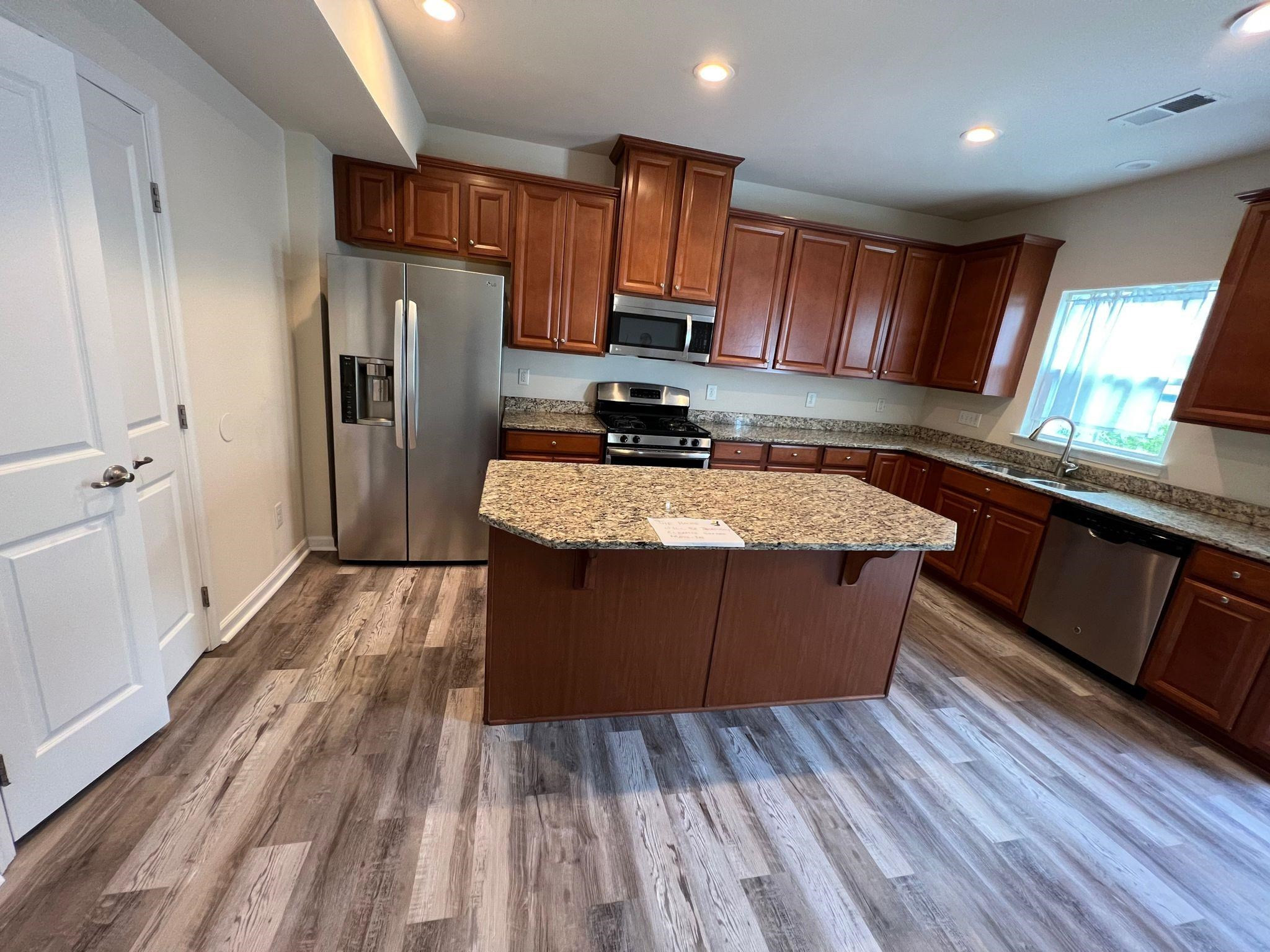 a large kitchen with wooden floors stainless steel appliances a sink and cabinets