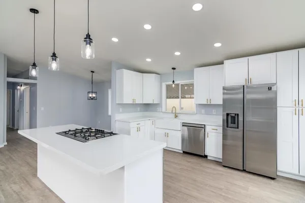 a kitchen with stainless steel appliances granite countertop a refrigerator a sink dishwasher a stove and white cabinets with wooden floor