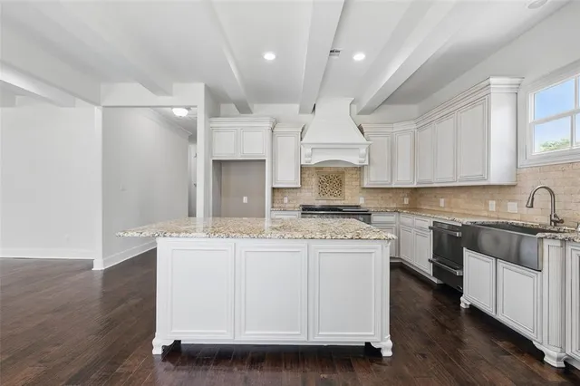 a kitchen with kitchen island granite countertop a stove a sink a refrigerator and white cabinets with wooden floor