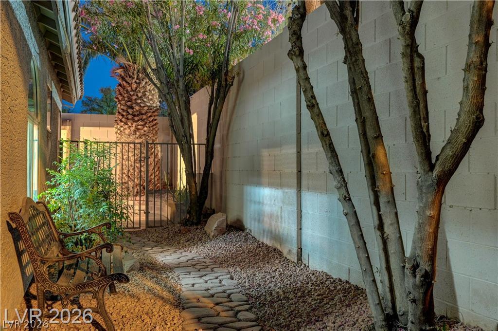 2283 Ramsgate Drive Henderson, NV 89074 - Photo 49 of 51 A stone paver pathway winds alongside a tall block wall under mature trees.