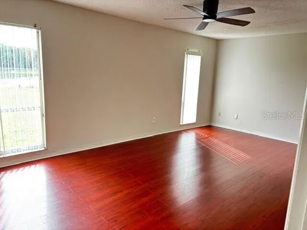 an empty room with wooden floor and windows with curtains