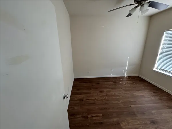 an empty room with a chandelier fan and wooden floor