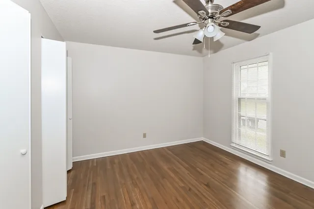 an empty room with wooden floor fan and windows