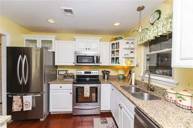 a kitchen with stainless steel appliances granite countertop a refrigerator a stove a sink dishwasher and white cabinets with wooden floor