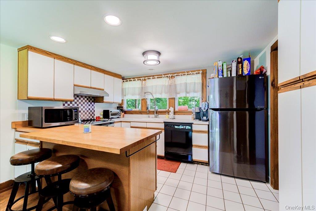 10-12 Woodlea Road Salt Point, NY 12578 - Photo 10 of 48 Kitchen featuring a wood-finish island with counter seating, white cabinetry with wood trim, white countertops, tile flooring, and a stainless steel range hood
