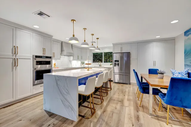 a kitchen with stainless steel appliances kitchen island granite countertop a table chairs a sink dishwasher a refrigerator and cabinets with wooden floor