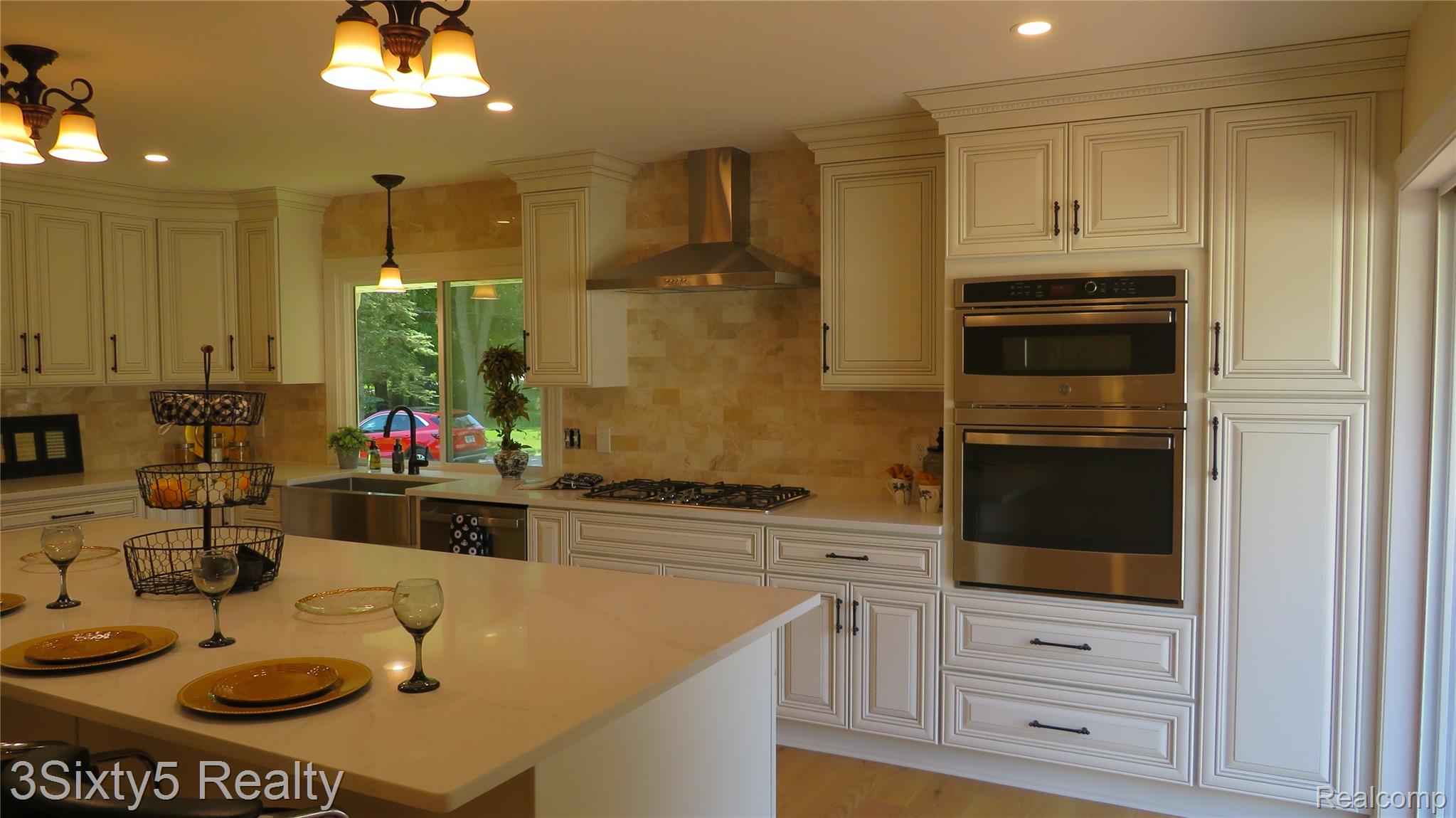 16558 Haggerty Road Belleville, MI 48111 - Photo 13 of 40 Spacious kitchen featuring an expansive island with a light-toned countertop, extensive white cabinetry, built-in stainless steel double ovens, a stainless steel range hood, and a tile backsplash