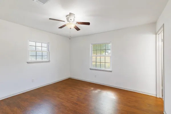 an empty room with wooden floor chandelier fan and windows