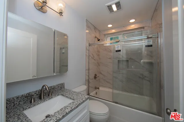 a bathroom with a granite countertop sink toilet a mirror and shower