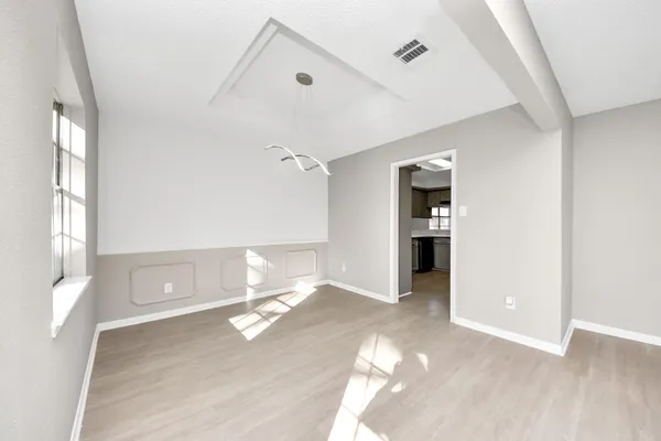 a view of empty room with wooden floor and kitchen