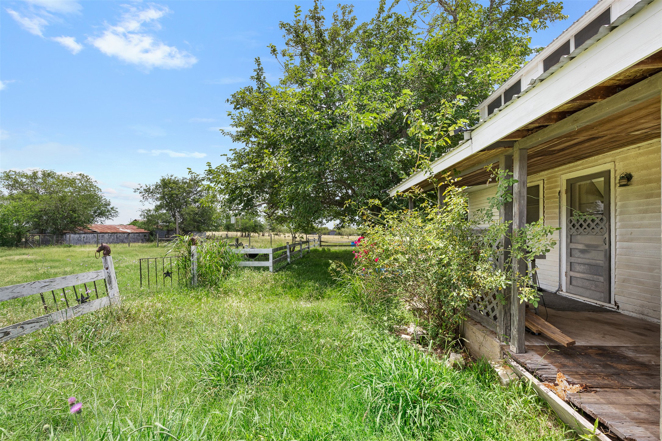 763 Upper Elgin River Road Elgin, TX 78621 - Photo 9 of 40 A charming weathered porch offers a peaceful retreat amidst sprawling green surroundings.