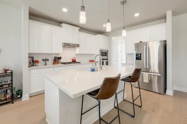 a kitchen with stainless steel appliances granite countertop a refrigerator a sink dishwasher a stove and white cabinets with wooden floor