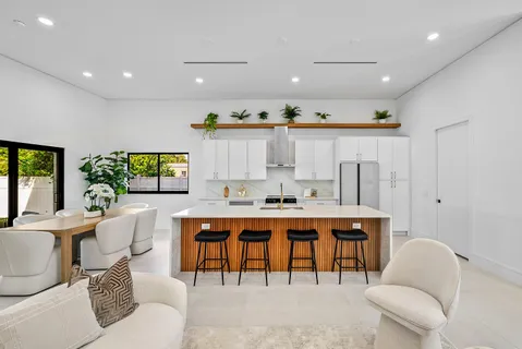 a large white kitchen with stainless steel appliances kitchen island granite countertop a refrigerator a sink dishwasher a dining table and chairs with wooden floor