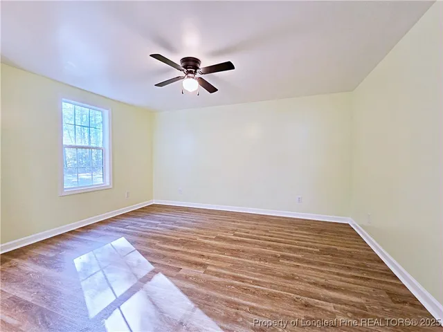 a view of empty room with wooden floor and fan