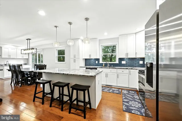 a kitchen with stainless steel appliances granite countertop a stove a refrigerator a sink a dining table and chairs with wooden floor