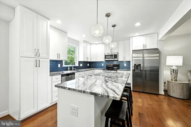 a kitchen with stainless steel appliances granite countertop a stove a sink a refrigerator a dining table and chairs with wooden floor