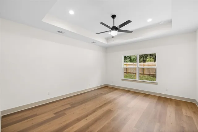 an empty room with wooden floor fan and windows