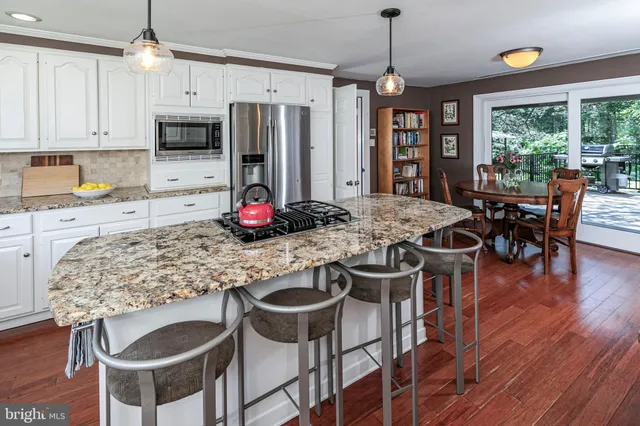 a kitchen with stainless steel appliances granite countertop a stove a refrigerator a kitchen island a dining table and chairs with wooden floor