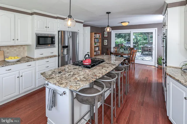 a kitchen with stainless steel appliances granite countertop a refrigerator a stove top oven a sink dishwasher and white cabinets with wooden floor