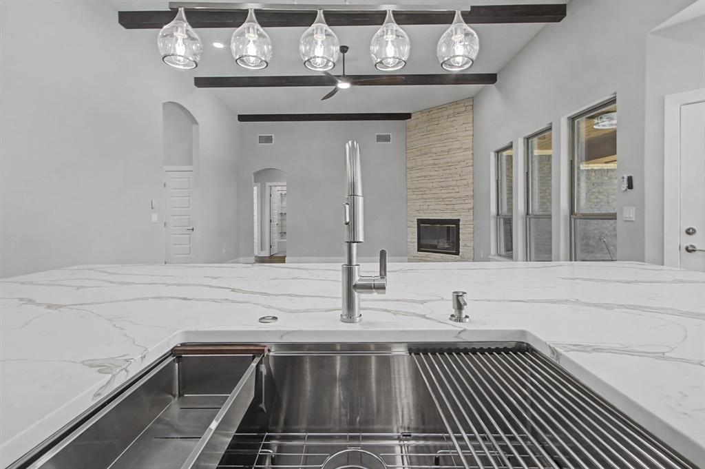 108 Winding Way Azle, TX 76020 - Photo 12 of 39 Kitchen view of light stone countertops, a stone fireplace, arched walkways, and beamed ceiling