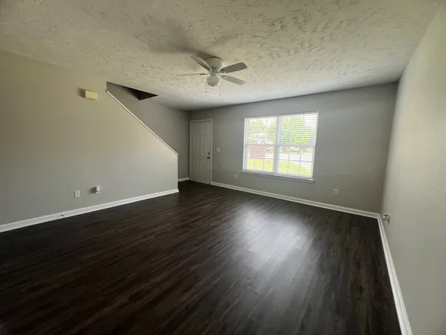 an empty room with wooden floor windows and fan