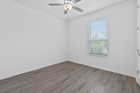 an empty room with wooden floor chandelier fan and windows