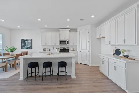 a kitchen with kitchen island granite countertop a sink a stove a refrigerator and white cabinets with wooden floor