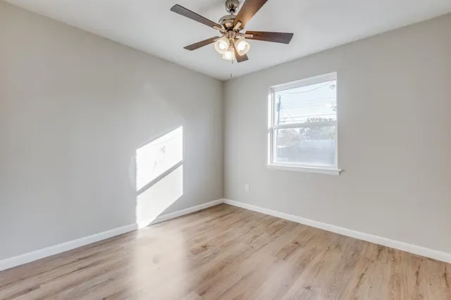 an empty room with wooden floor windows and fan
