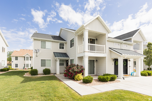 Multi-unit residence featuring light-colored siding, dark shingle roofing, a second-story balcony with white railing, and covered entryways