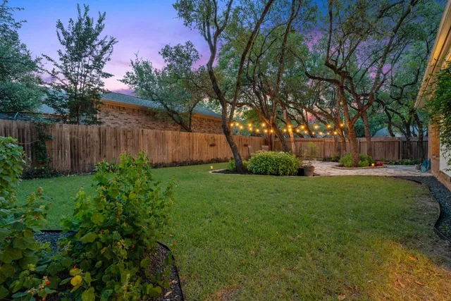 a view of a backyard with large trees and wooden fence