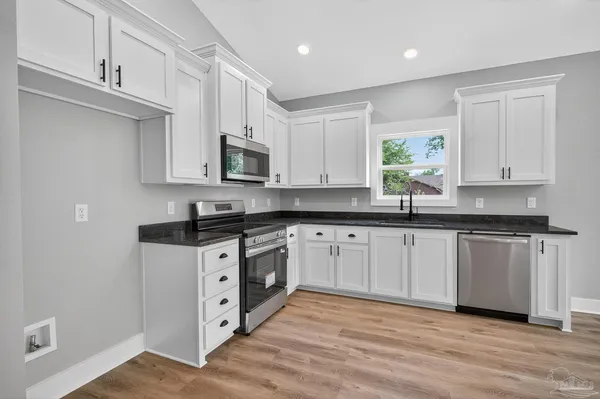 a kitchen with stainless steel appliances granite countertop white cabinets sink and window