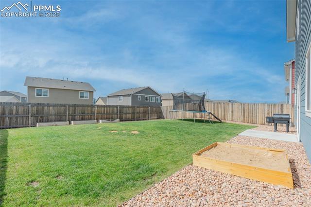 11053 Avena Road Peyton, CO 80831 - Photo 12 of 27 Fenced backyard featuring a trampoline, a residential view, and a vegetable garden
