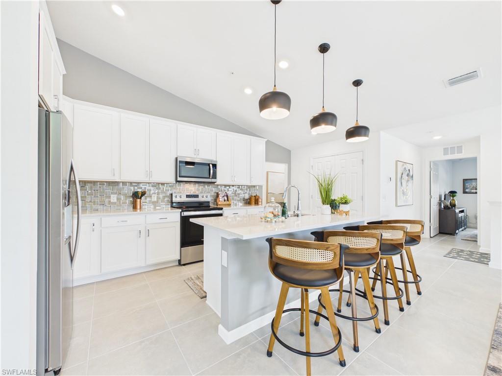 5683 Mayflower Way, Unit 908 Ave Maria, FL 34142 - Photo 2 of 37 Kitchen with stainless steel appliances, a kitchen breakfast bar, vaulted ceiling, an island with sink, and white cabinetry