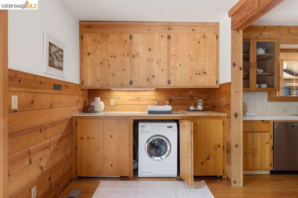 287 Purdue Avenue Kensington, CA 94708 - Photo 27 of 60 Laundry station featuring wood-paneled walls and cabinetry, under-cabinet lighting, a built-in sink, and a front-loading appliance
