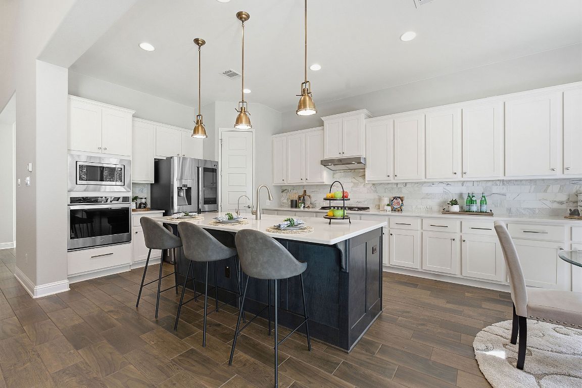 4020 Logan Ridge Drive Cedar Park, TX 78613 - Photo 12 of 40 Kitchen with backsplash, a kitchen bar, appliances with stainless steel finishes, hanging light fixtures, and white cabinets
